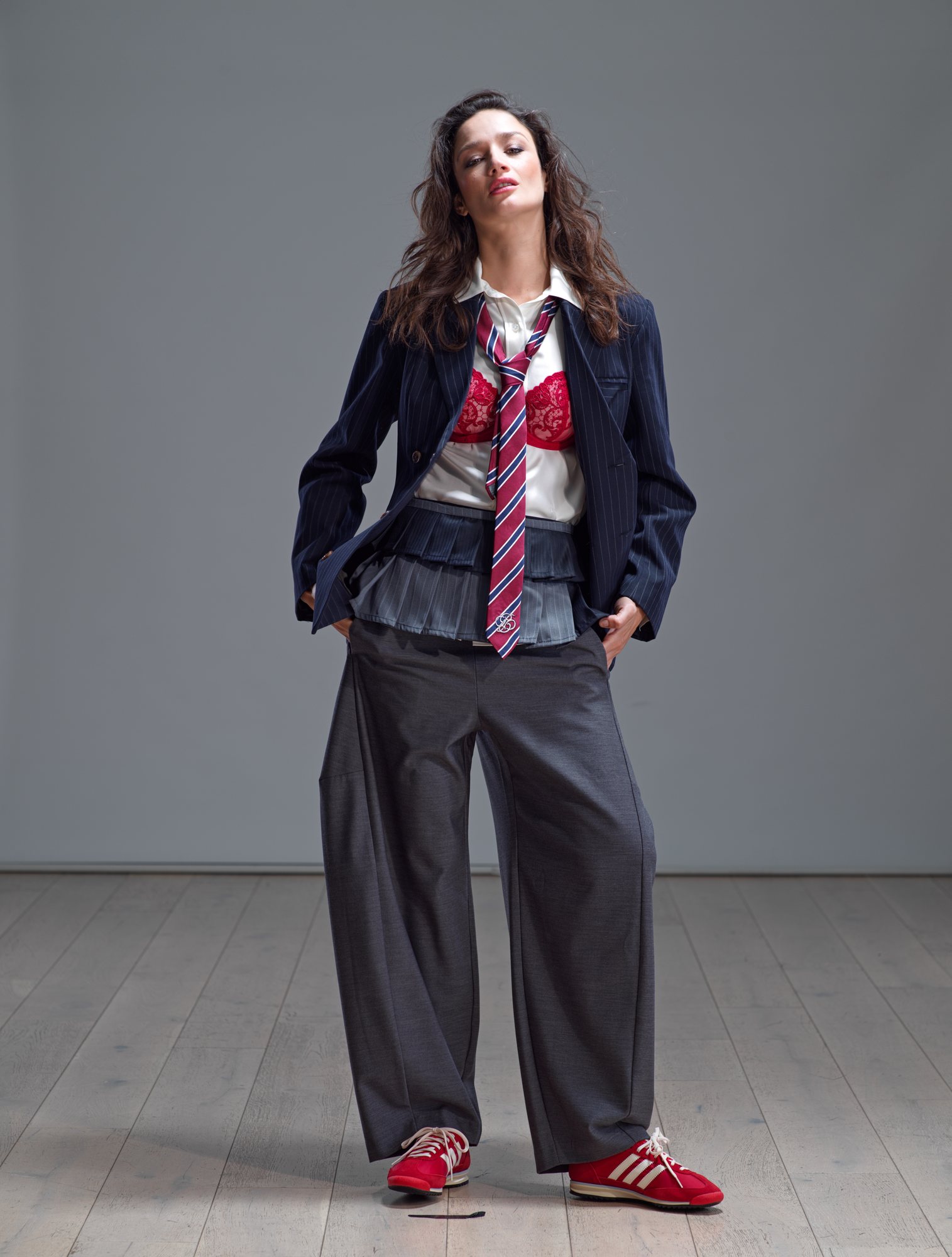 Model in a navy pinstripe blazer, white shirt and red striped tie, with grey wide-leg trousers and red trainers