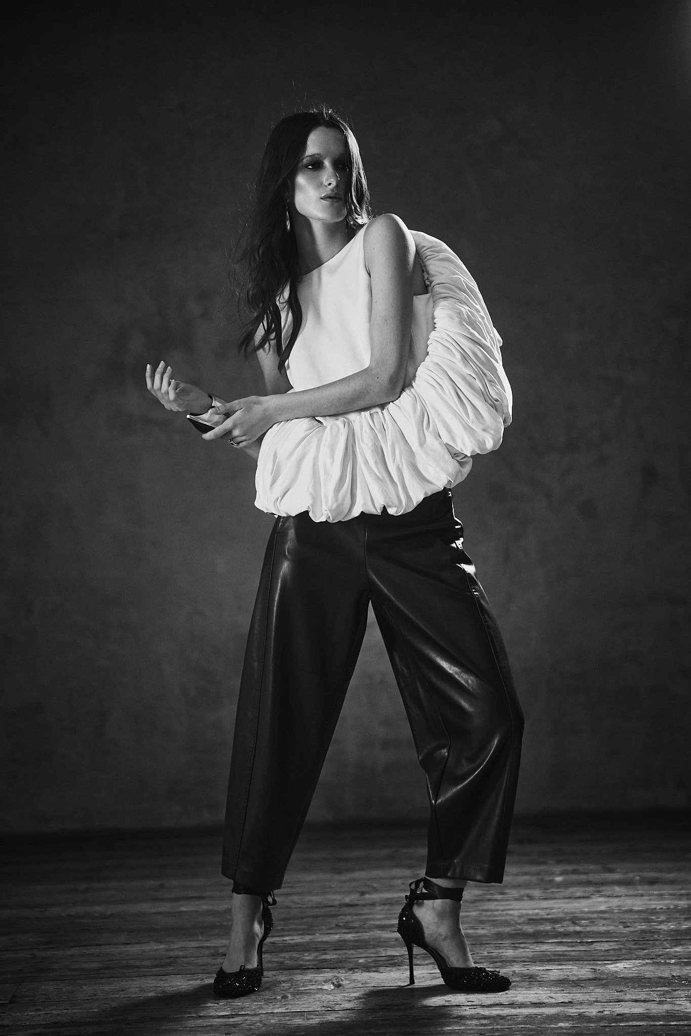 Black and white fashion portrait of a model in a white sculptural ruched top and black leather trousers