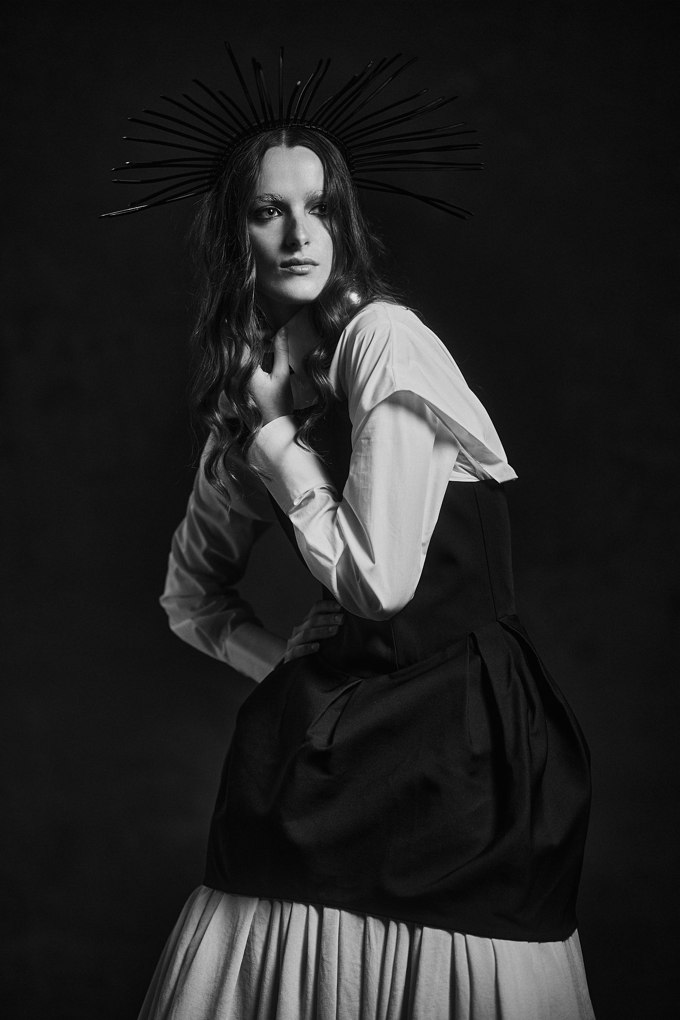Black and white portrait of a model in a spiked halo headpiece, white shirt and black structured dress