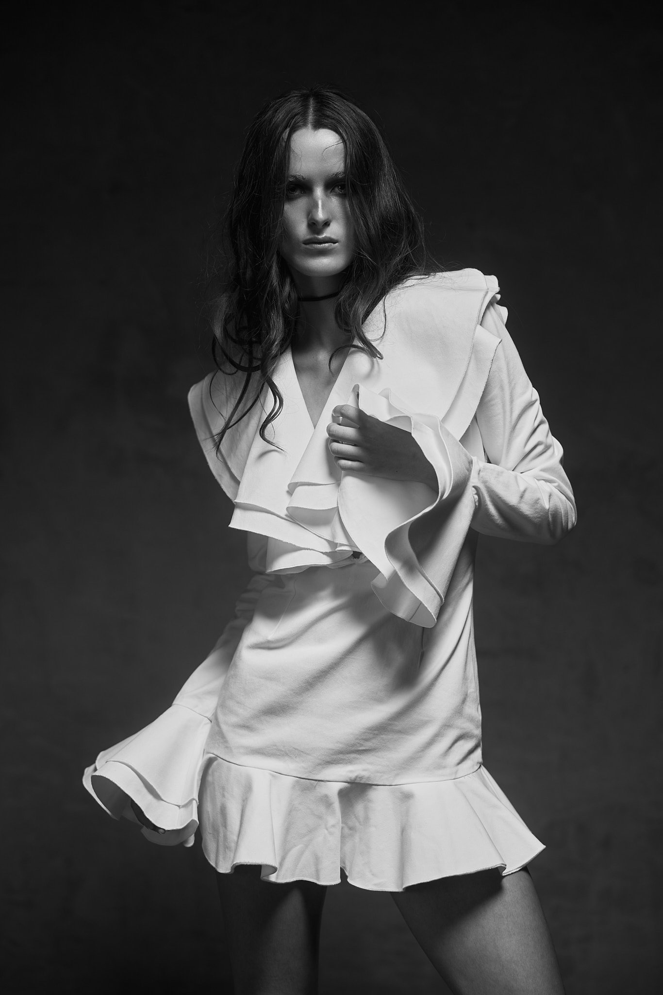 Black and white portrait of a model in a white ruffled mini dress with flared sleeves and a black choker
